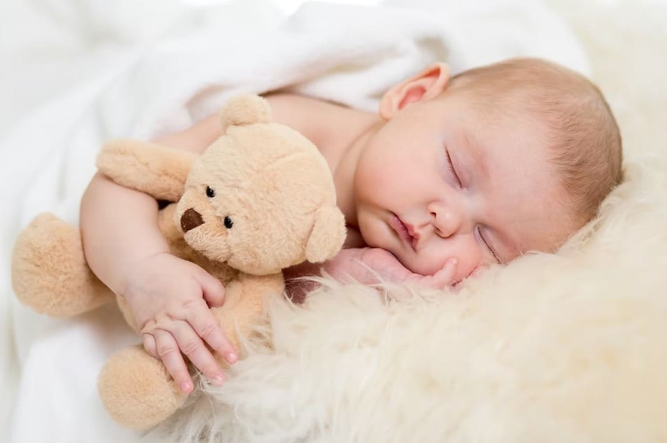 sleeping baby against a pillow holding a teddy bear